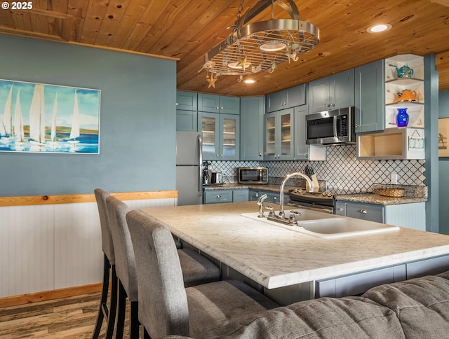 5353 SW Neal Ave, Waldport, OR 97394 - kitchen with appliances with stainless steel finishes, wood ceiling, wood finished floors, decorative backsplash, and glass insert cabinets