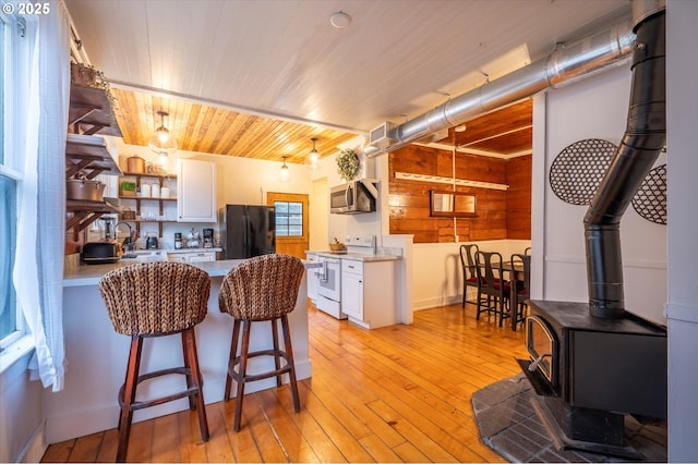 kitchen with electric stove, freestanding refrigerator, a wood stove, light countertops, and white cabinetry