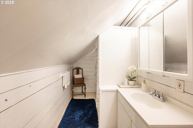 bathroom featuring wooden walls, vaulted ceiling, and vanity