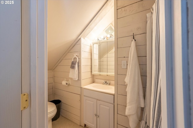 bathroom featuring lofted ceiling, wood walls, vanity, and toilet