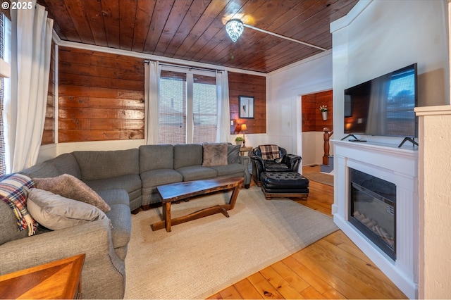 living area with hardwood / wood-style floors, wood walls, wooden ceiling, and a glass covered fireplace