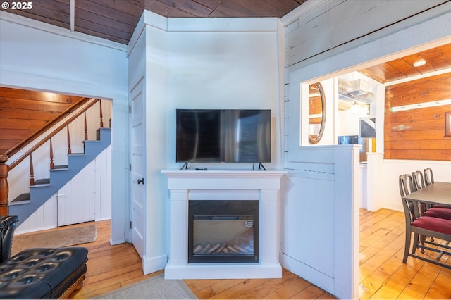 living room with wooden walls, wood ceiling, stairway, light wood finished floors, and a glass covered fireplace