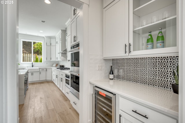 11723 NW Sadie St, Portland, OR 97229 - bar area featuring beverage cooler, light wood-type flooring, a sink, backsplash, and double oven
