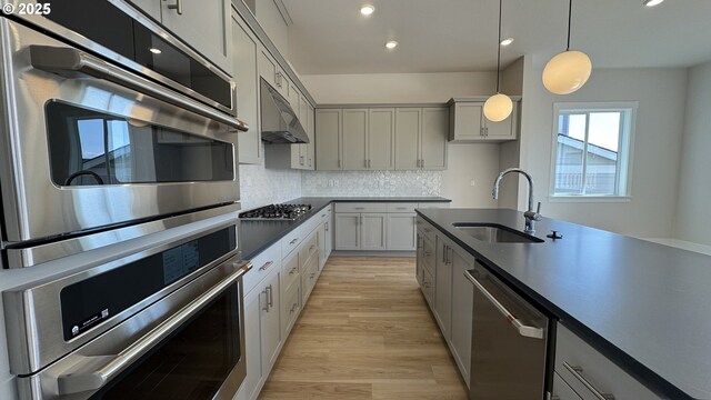 11699 SW 178th Dr, Beaverton, OR 97007 - kitchen featuring stainless steel appliances, under cabinet range hood, dark countertops, hanging light fixtures, and light wood finished floors