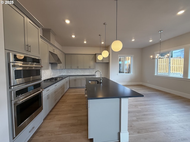 kitchen featuring decorative backsplash, dark countertops, appliances with stainless steel finishes, under cabinet range hood, and a sink