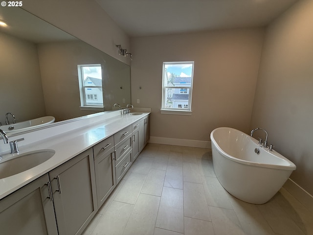 bathroom with double vanity, a soaking tub, baseboards, and a sink