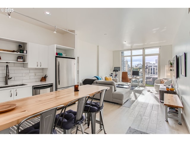 kitchen with appliances with stainless steel finishes, open shelves, light wood-type flooring, a sink, and a breakfast bar