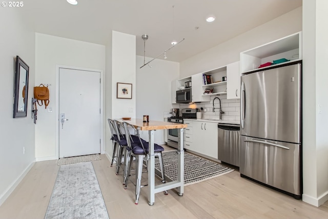 1255 NW 9th Ave Unit 806, Portland, OR 97209 - kitchen with white cabinets, open shelves, light wood-style floors, stainless steel appliances, and decorative backsplash