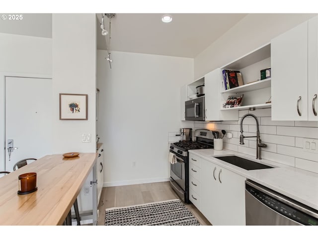 kitchen with open shelves, appliances with stainless steel finishes, a sink, white cabinetry, and backsplash