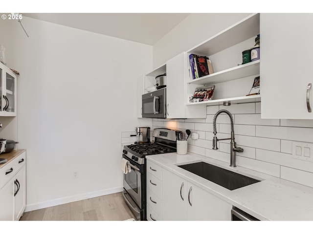 kitchen featuring tasteful backsplash, light stone countertops, light wood-type flooring, a sink, and stainless steel gas range