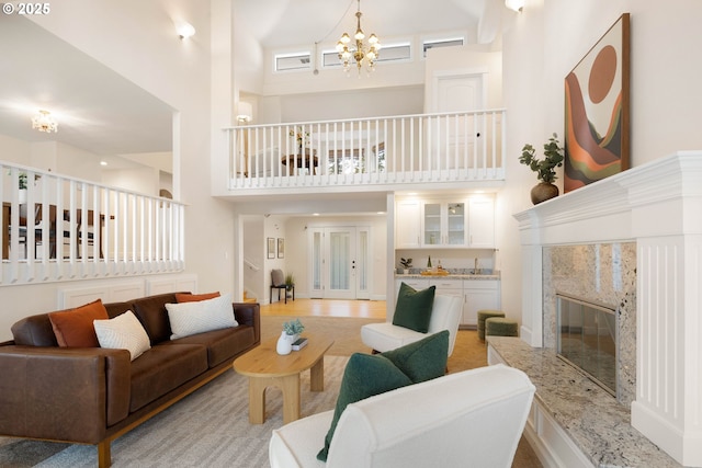 living room with a high ceiling, a premium fireplace, a notable chandelier, and light wood-type flooring