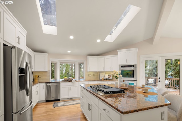 kitchen featuring lofted ceiling with skylight, white cabinetry, dark stone countertops, a kitchen island, and stainless steel appliances