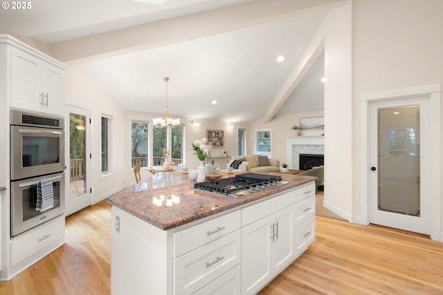 kitchen featuring vaulted ceiling with beams, light stone counters, a kitchen island, stainless steel appliances, and white cabinets