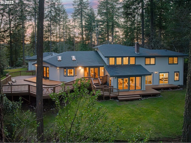 back house at dusk featuring a wooden deck and a lawn