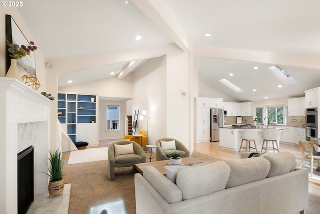 living room with sink, a skylight, high vaulted ceiling, beam ceiling, and light hardwood / wood-style floors