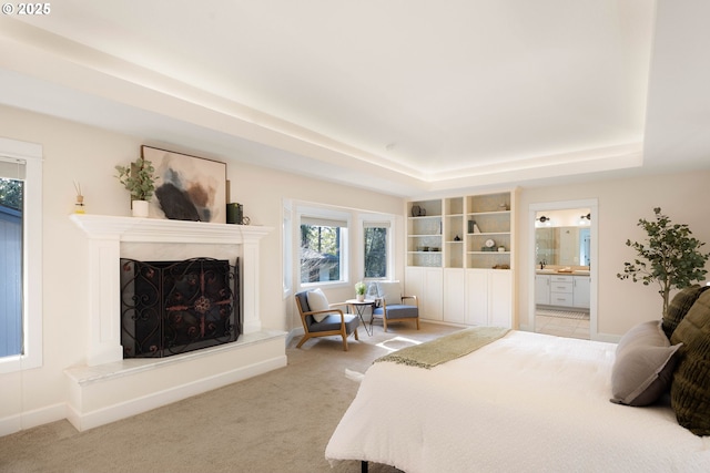 carpeted bedroom with a high end fireplace, a tray ceiling, and connected bathroom