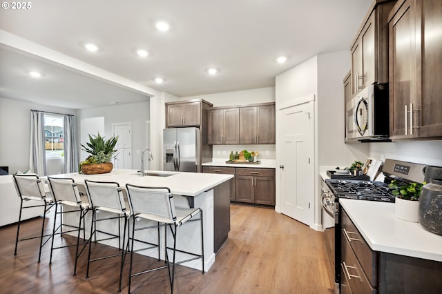 kitchen with a sink, stainless steel appliances, a breakfast bar, a center island with sink, and light wood finished floors