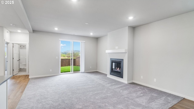 unfurnished living room featuring light wood-style flooring, baseboards, a glass covered fireplace, and recessed lighting