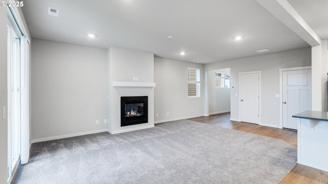 unfurnished living room featuring wood finished floors, visible vents, recessed lighting, baseboards, and a glass covered fireplace
