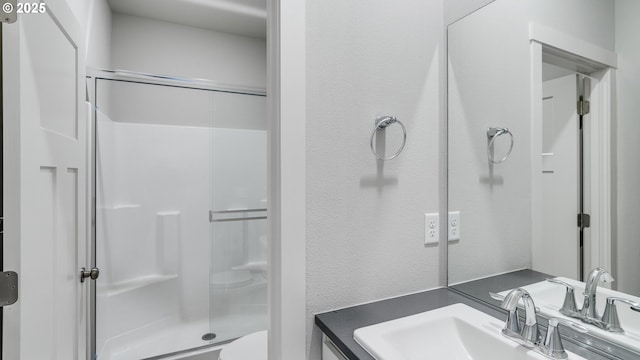 bathroom with a stall shower, vanity, toilet, and a textured wall
