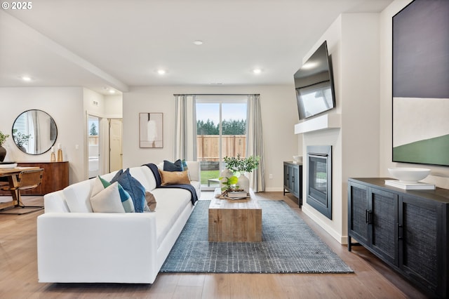 living room with recessed lighting, a glass covered fireplace, and wood finished floors