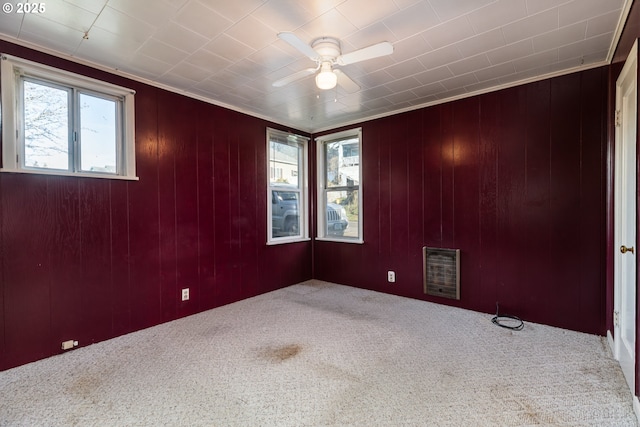 empty room with heating unit, ornamental molding, wooden walls, carpet flooring, and ceiling fan