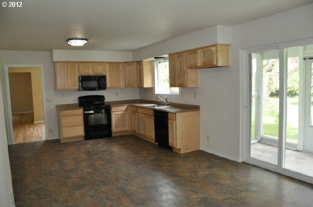 kitchen with black appliances, light countertops, a sink, and light brown cabinetry