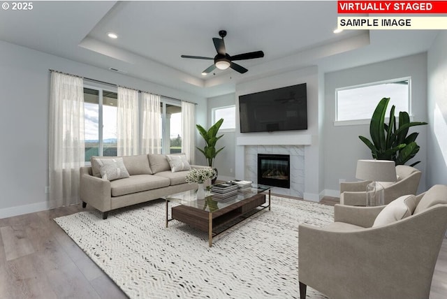 living room featuring a raised ceiling, a tiled fireplace, a healthy amount of sunlight, and hardwood / wood-style floors