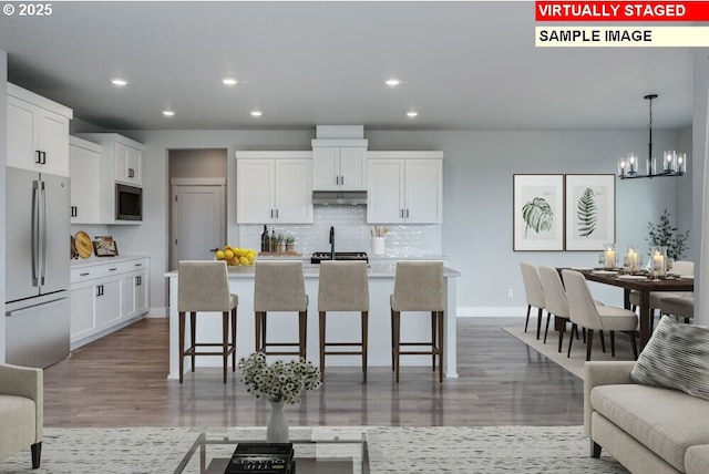 kitchen featuring built in microwave, an island with sink, white cabinets, stainless steel fridge, and a kitchen breakfast bar