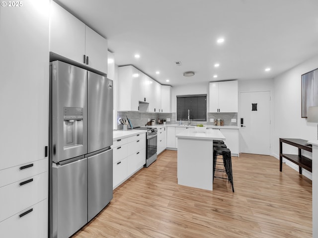 kitchen featuring white cabinets, a breakfast bar area, backsplash, a kitchen island, and appliances with stainless steel finishes