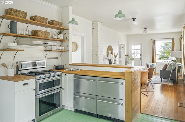 kitchen with butcher block countertops, white cabinetry, hanging light fixtures, ventilation hood, and range with two ovens