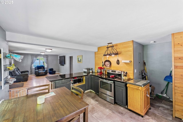 kitchen with appliances with stainless steel finishes, wooden walls, light wood-style floors, dark countertops, and open floor plan