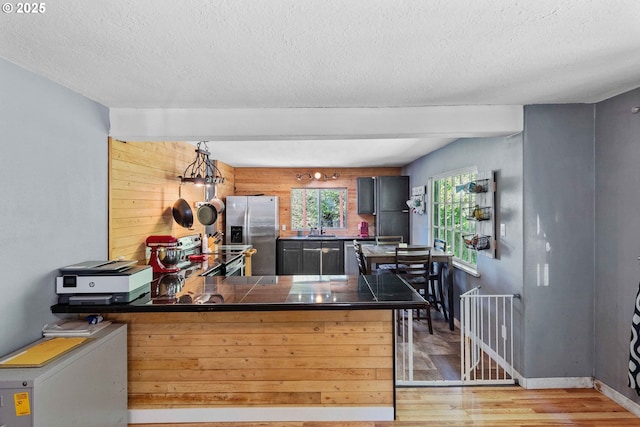 kitchen featuring stainless steel appliances, a peninsula, light wood finished floors, a textured ceiling, and a sink
