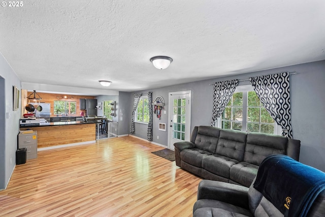 living room with light wood-type flooring, plenty of natural light, a textured ceiling, and baseboards