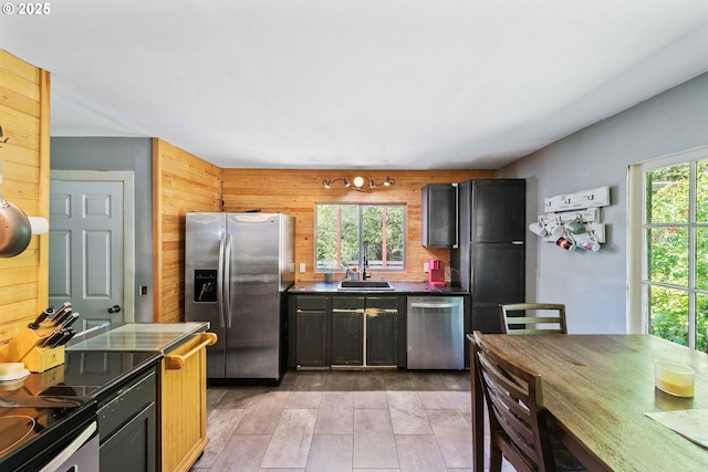 kitchen featuring stainless steel appliances, a sink, dark countertops, wooden walls, and light wood finished floors