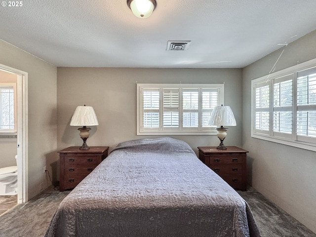 bedroom featuring connected bathroom, carpet, visible vents, and a textured ceiling