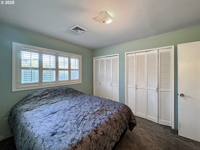 carpeted bedroom with visible vents, multiple closets, and a textured ceiling