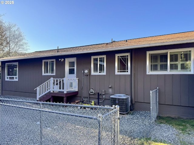 view of front facade featuring board and batten siding, central AC, roof with shingles, and fence