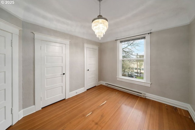 unfurnished bedroom featuring hardwood / wood-style floors, baseboard heating, and a chandelier