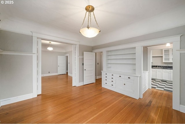 unfurnished dining area featuring built in shelves, sink, and light wood-type flooring