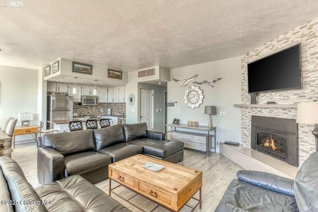 living room with visible vents, a textured ceiling, light wood finished floors, and a fireplace