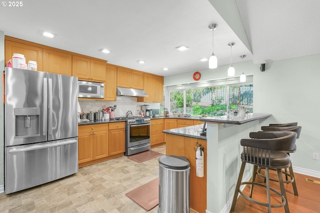 10145 SW Paulina Dr, Tualatin, OR 97062 - kitchen featuring a peninsula, under cabinet range hood, a breakfast bar area, decorative backsplash, and appliances with stainless steel finishes