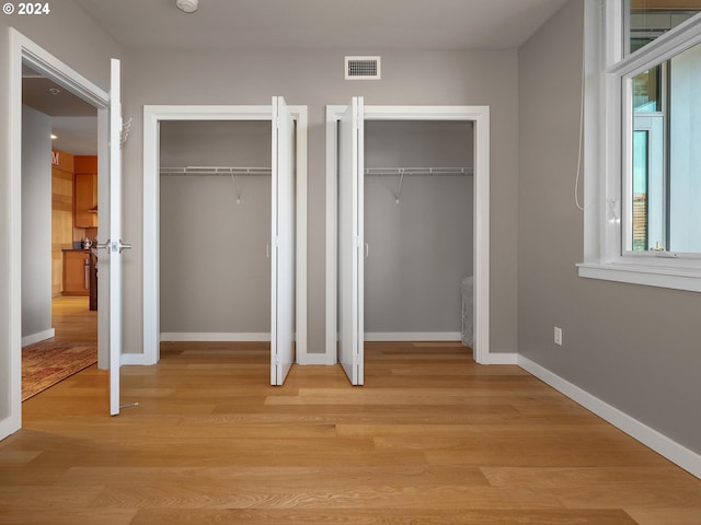 unfurnished bedroom with light hardwood / wood-style floors and multiple closets