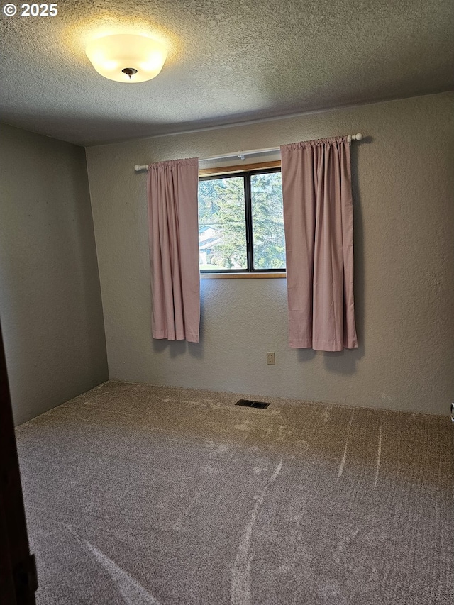 spare room with carpet flooring, a textured wall, visible vents, and a textured ceiling