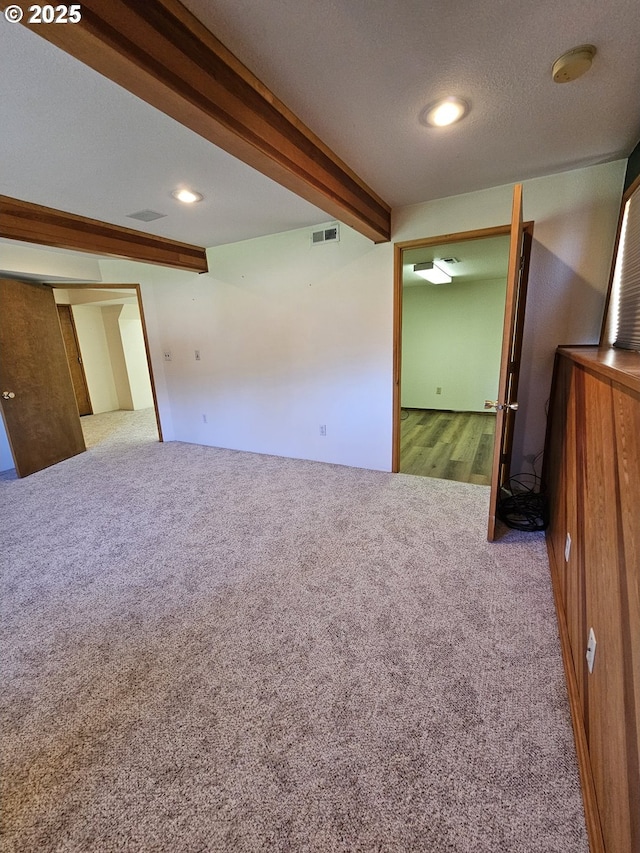 empty room featuring beam ceiling, visible vents, a textured ceiling, and carpet