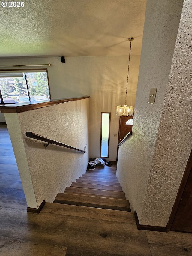 stairway with an inviting chandelier, a textured wall, and a textured ceiling