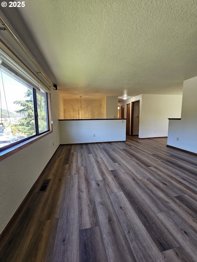 unfurnished living room featuring baseboards, visible vents, dark wood-style flooring, and a textured ceiling