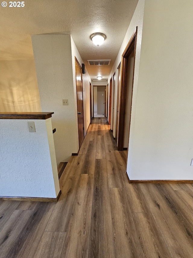 corridor with dark wood finished floors, visible vents, a textured ceiling, and baseboards