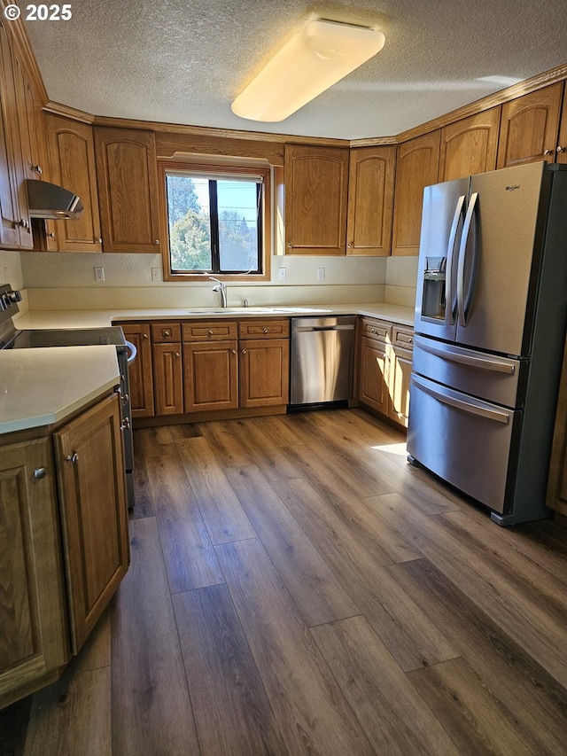 kitchen featuring a sink, appliances with stainless steel finishes, brown cabinetry, and dark wood-style flooring