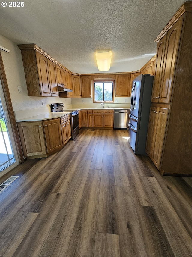 kitchen featuring dark wood-style flooring, a sink, light countertops, appliances with stainless steel finishes, and brown cabinets